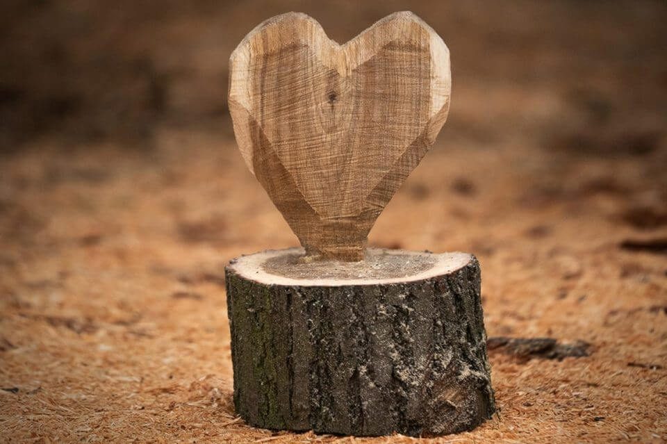 Cœur en bois sculpté posé sur un morceau de bois dans un environnement naturel.